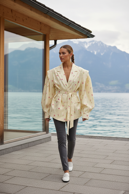 Native Swiss woman wearing the floral print yellow oversized belted blazer by a Swiss lakeside pavilion